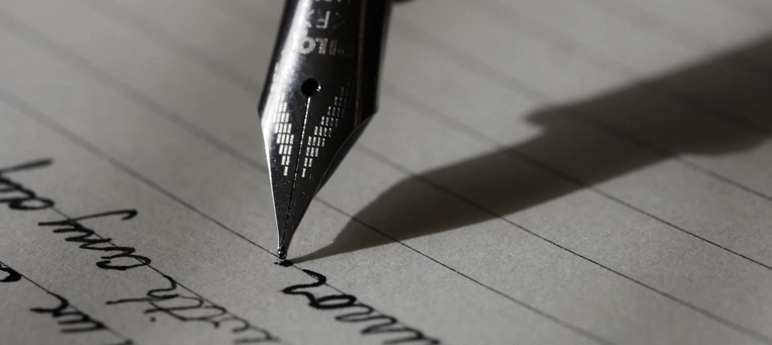 Plumín de una estilográfica sobre una carta manuscrita, en penumbra