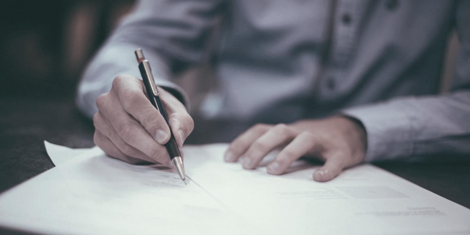 Manos escribiendo sobre unos folios en una mesa oscura